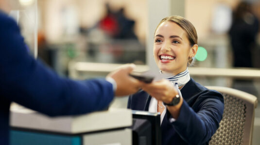 Woman, airport and service agent with passport helping traveler for check in at terminal counter. Female passenger assistant with smile in travel security or immigration documents for airline control.